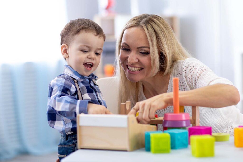 Cute kid and teacher playing with toys at home. Little boy having fun pastime in nursery.
